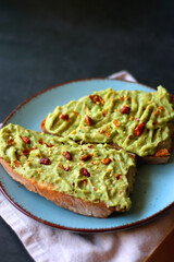 Turquoise plate with two pieces of avocado toast on dark background. Selective focus.