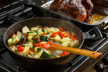 A frying pan with stewed vegetables on a plate next to a tray with baked chicken.