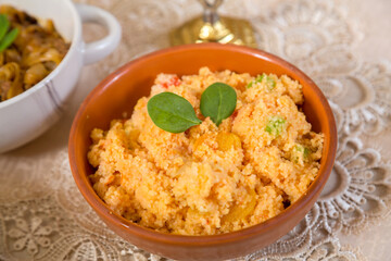 Couscous with dried fruits garnished with herbs in a clay plate on a tablecloth.