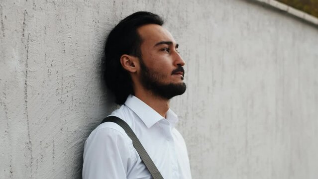 Portrait of a young asian businessman in a white shirt standing near the wall outdoor with a disappointed face worrying about difficult decisions to make in business