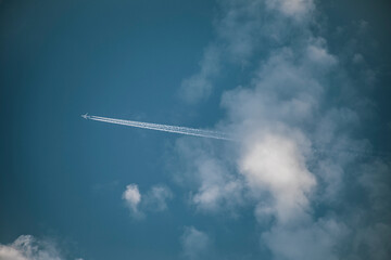 Blue sky with clouds from which a commercial airplane appears leaving a white trail