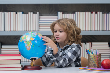 School child looking at globe in library at the elementary school. Little student school child. Portrait of nerd student with school supplies. World globe.