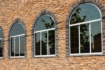 Beautiful arched windows in building, view from outdoors. White painted wood arched window in a red stone wall