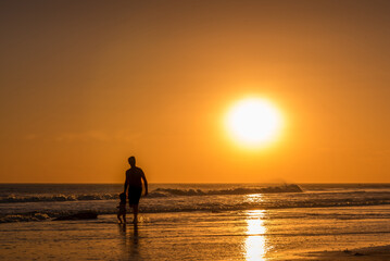 Man walking with a girl along the seashore on the beach at sunset.