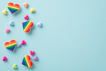 Symbolic LGBTQ+ accessories like rainbow-colored heart pins seen from above on a pastel blue background, with plenty of space for text or advert