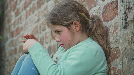 Upset Frustrated Depressed Young Caucasian Girl Sitting Alone Outdoors Against Brick Wall Hiding from People Parents and Friends