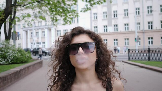young woman portrait walks closely around the city and smokes an electronic cigarette 4k slow motion