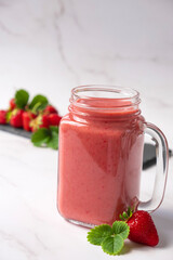 Strawberry smoothie or milkshake with fresh strawberry fruit and green leaves on marble background. Recipe of strawberry drink in jar mug full of vitamins and antioxidants.