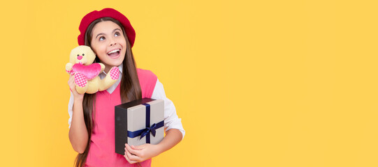 happy teen girl in french beret hold toy present and gift box on yellow background, wow. Kid girl with gift, horizontal poster. Banner header with copy space.
