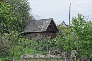 one old brown wooden rural house under a gray slate roof among green vegetation and trees on the street against the sky