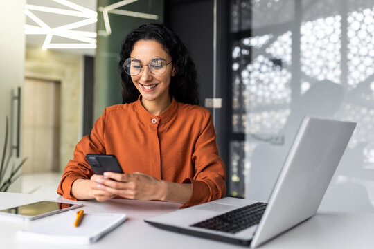 Young successful hispanic woman inside office at workplace using online application on phone, businesswoman successful and satisfied with work and achievement results in glasses browsing internet.