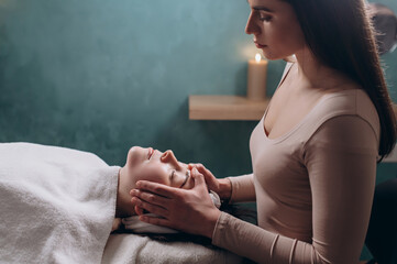 The beautician makes a deep facial massage to a young woman. Face massage technique against aging. 