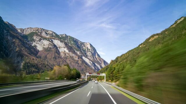 Daytime timelapse of POV highway traffic in Austrian mountains during autumn. Cloudy sky above picturesque mountain range offers a scenic journey in the Alps.