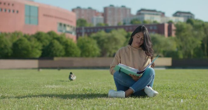 Young teenage Latina college student studying for an exam in an outdoor park with books