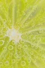 Close-up of a lime slice in liquid with bubbles. Slice of ripe lime in water. Close-up of fresh lime slice covered by bubbles. Macro vertical image.