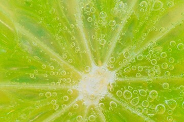 Close-up of a lime slice in liquid with bubbles. Slice of ripe lime in water. Close-up of fresh lime slice covered by bubbles. Macro horizontal image.