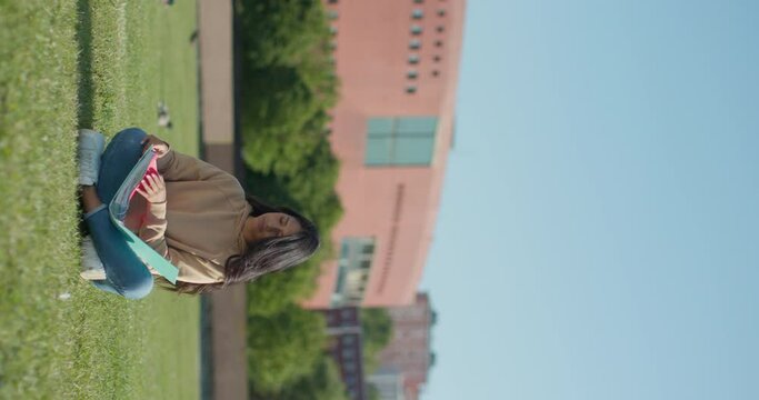 Young teenage Latina college student studying for an exam in an outdoor park with books, vertical shot