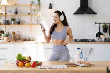 Brunette smiling fit woman wearing sportswear listening music preparing dinner
