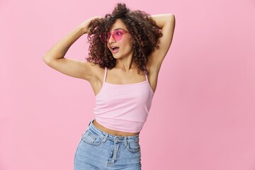 Happy woman afro curls hair dancing on a pink background in summer pink t-shirt jeans and glasses, summer vibe, copy space