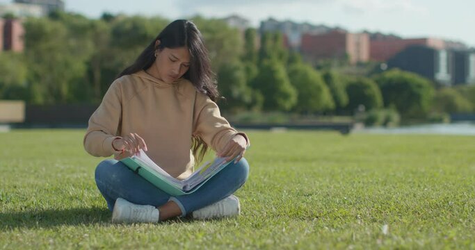 Young teenage Latina college student studying for an exam in an outdoor park with books
