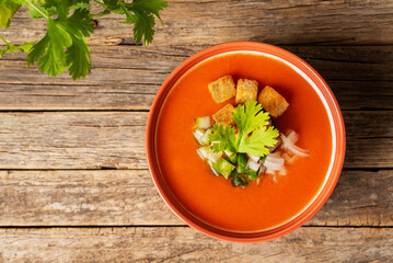Bowl with gazpacho and pieces of vegetables, on a rustic old wooden table, top view.