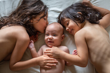 two elder sisters kissing smiling newborn sister