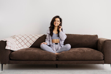 Obraz premium Portrait of smiling latin woman wearing stylish pyjama's sitting on sofa