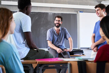 Secondary student being helped by professor in classroom. Malee caucasian teacher helping guys during after class. High school girls and boys talking for explanations to helpful. . High quality photo - obrazy, fototapety, plakaty