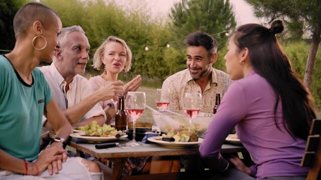 Happy family eating and drinking red wine at dinner barbecue party outside. Mature and young people dining together on backyard. Youth and elderly weekend lifestyle activities. High quality photo