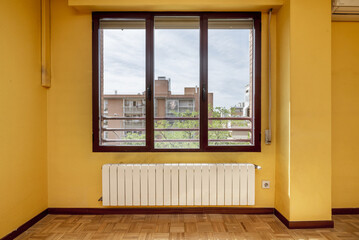 An empty room with mustard yellow painted walls, a light oak parquet wooden floor, an aluminum window