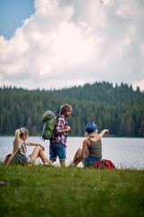 Friends with backpacks look at beautiful lake at hiking