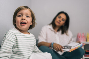 Mother sitting on the bed looking at her blonde son who is nervous and excited because he is going to read his favorite story.