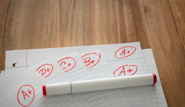 Different grades school paper marked in red ink over a wood desktop. Test results concept. Pass exam.