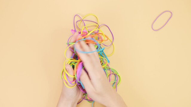 Hands taking bunch of colorful rubber bands and squizzing them on yellow background. Bright office rubber bands. Multicolored elastic rubber bands close up.