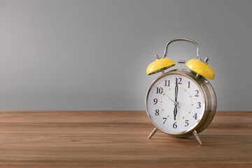 Retro silver alarm clock. 6:00.  am,  pm. Neutral background. Brown wood surface. Horizontal  photography with empty space for text or image.