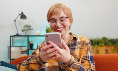Oh my God Wow. Excited happy joyful winner young woman use smartphone typing browsing found out great win good news celebrate victory. Girl with mobile phone sitting at home apartment in room on couch