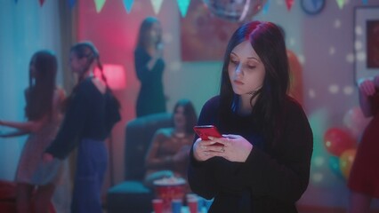 Goth girl watching video on phone, typing a message, checking social media while her friends are...