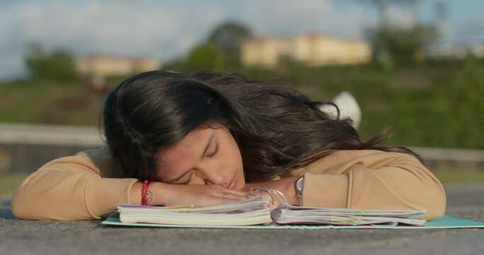 Young teenage Latina college student studying for an exam in an outdoor park with books