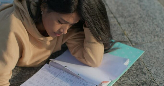 Young teenage Latina college student studying for an exam in an outdoor park with books