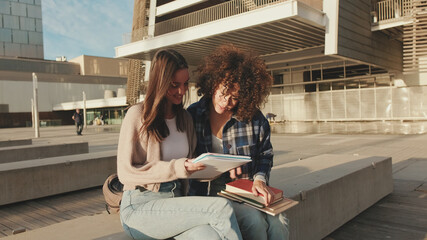 Student girls chatting and laughing sitting outside. Girls share news and have fun sitting next to...