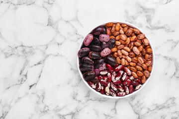 Different kinds of dry kidney beans in bowl on white marble table, top view