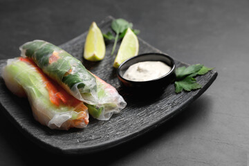 Delicious rolls wrapped in rice paper served on black table, closeup