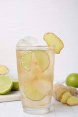 Glass of tasty ginger ale with ice cubes and ingredients on white tiled table