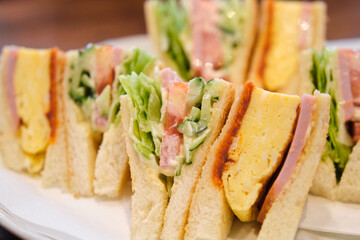 Japanese sandwich with omelette, ham, tomato, lettuce, cucumber and sauces in a cafeteria.