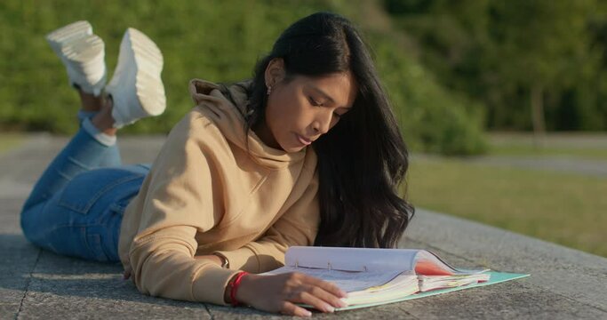 Young teenage Latina college student studying for an exam in an outdoor park with books