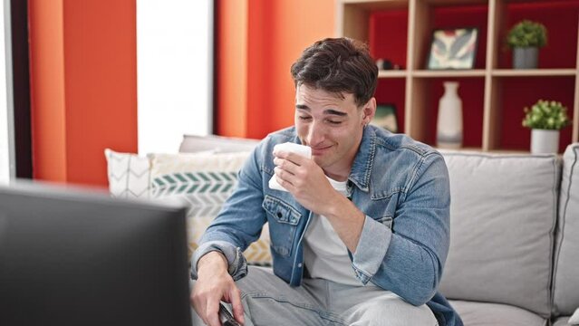 Young hispanic man watching sad movie sitting on sofa with crying at home