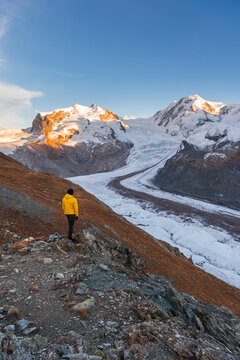 Hiker stands on rocks admiring Monte Rosa massif, Gorner Glacier (Gornergletscher) and Lyskamm peaks at sunset, Riffealp, Zermatt, canton of Valais, Swiss Alps, Switzerland
