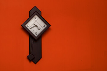 Wooden squire clock with pendulum hanging on a orange wall