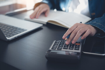 Business woman calculating monthly expenses, managing budget. Woman sitting at table using calculator to calculate tax refund, working at office with laptop computer on table, close up