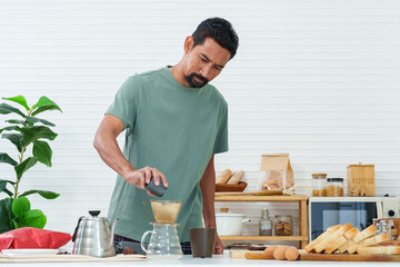 Close up hand of asian man pouring ground coffee beans Into the cup placed on the jug for drip coffee In the morning of the day before work Get ready to drink with breakfast. alone in kitchen